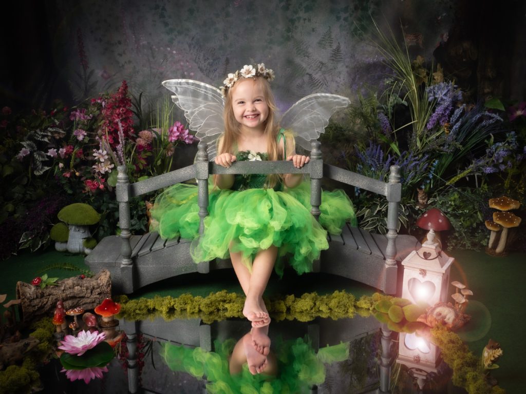Little girl in a magical green fairy dress sat on a bridge