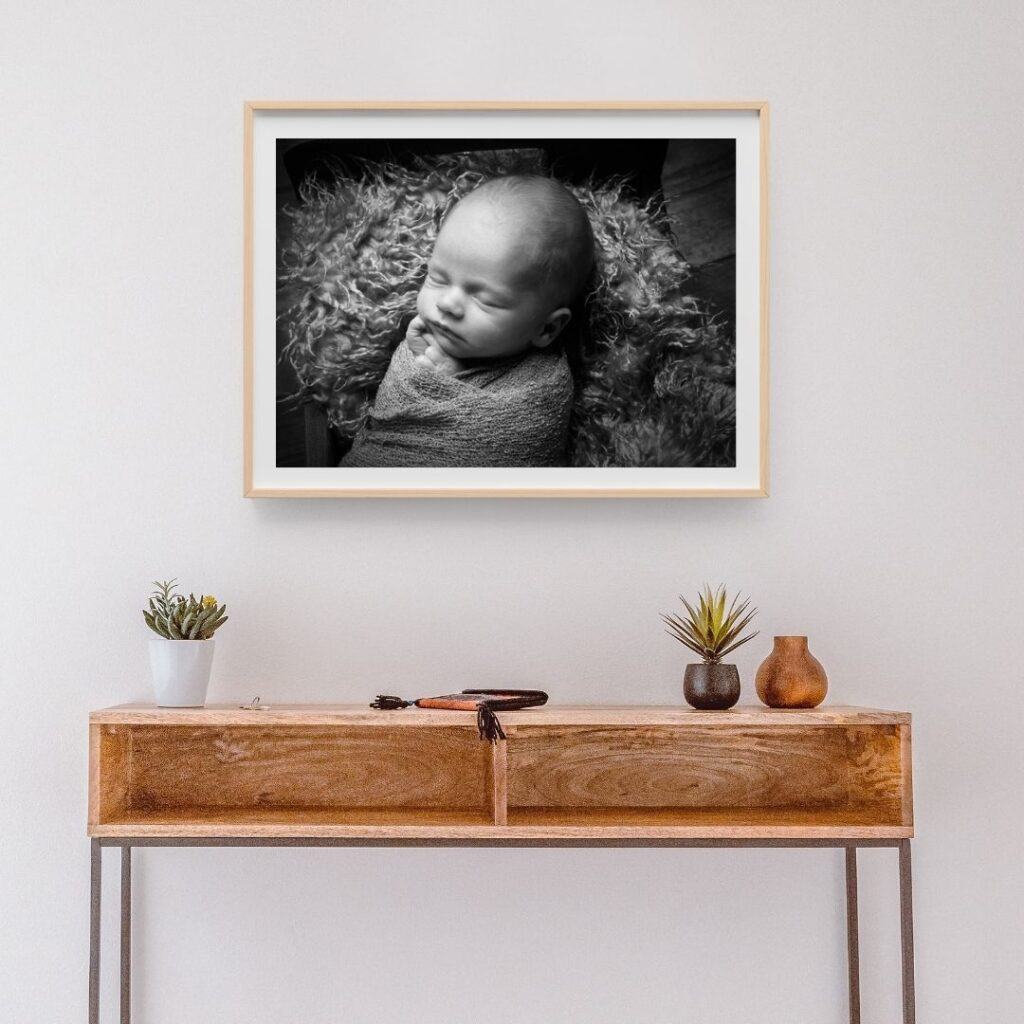 Framed black and white newborn photo print displayed above a wooden console table in a home interior setting