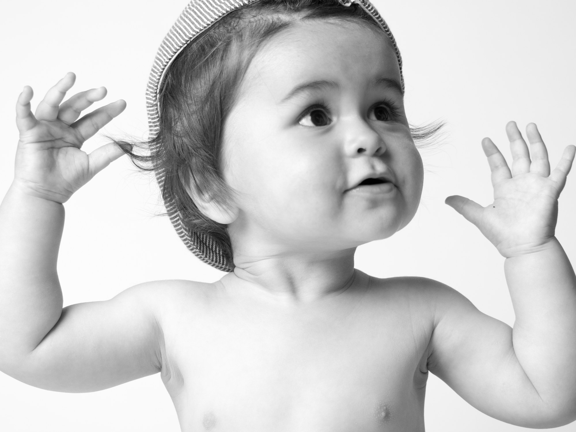 Baby in a striped hat with hands raised, black and white