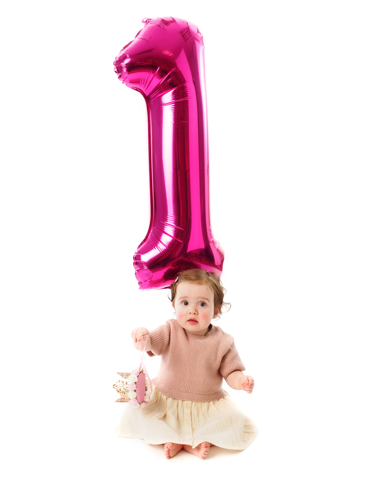 One-year-old sitting under a pink number one balloon