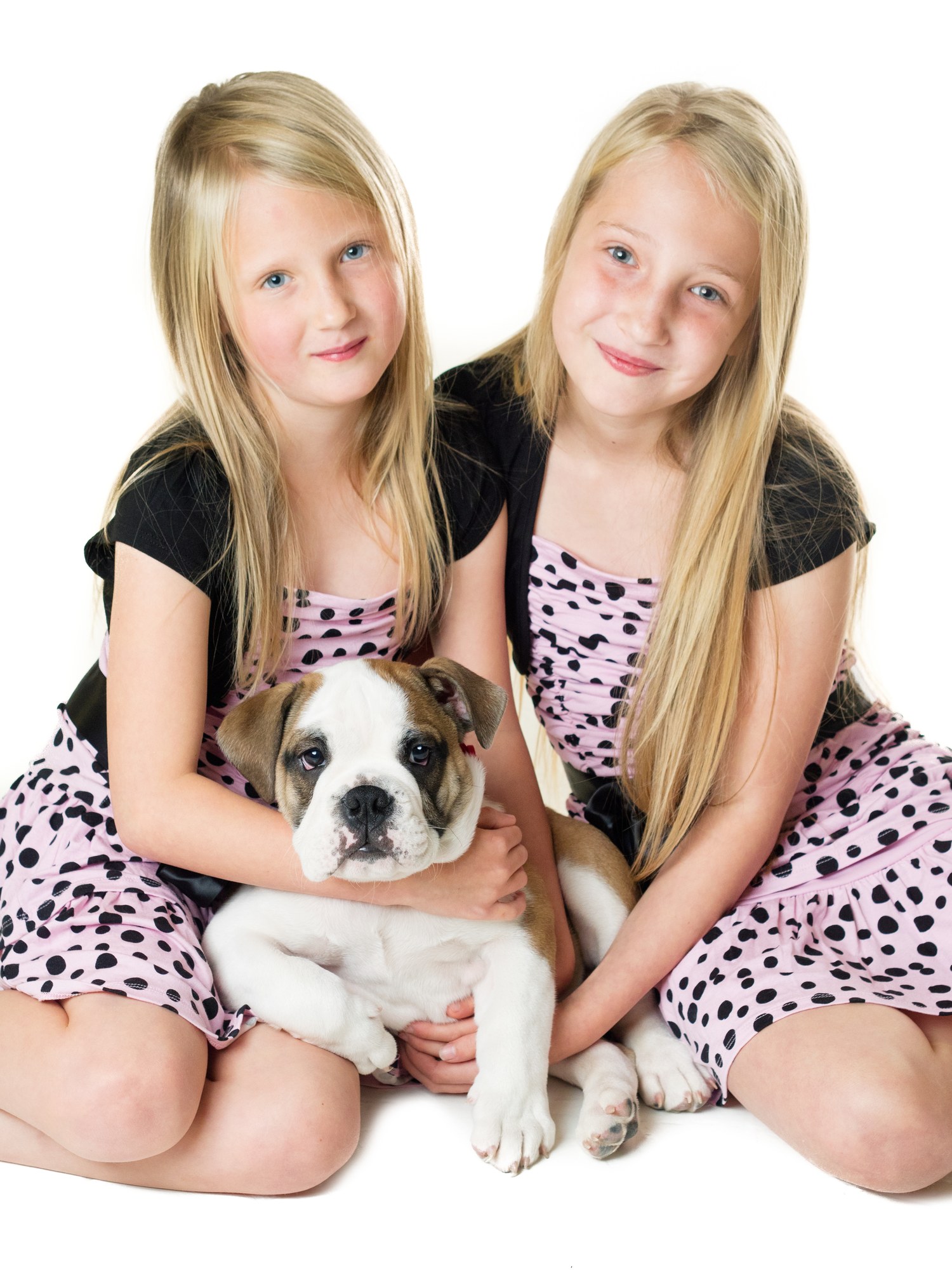 Twin sisters cuddling a bulldog puppy