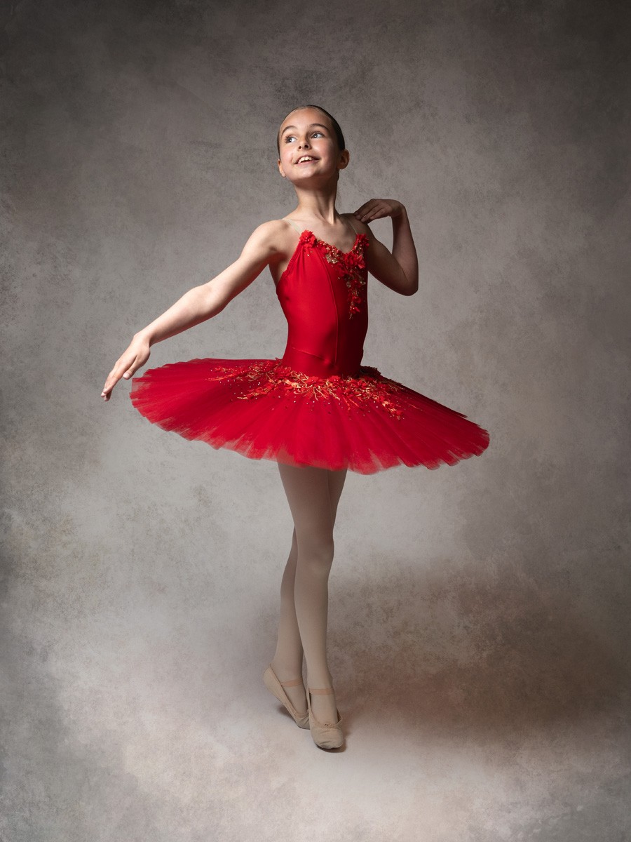 Smiling ballerina in a red tutu posing on a painted backdrop
