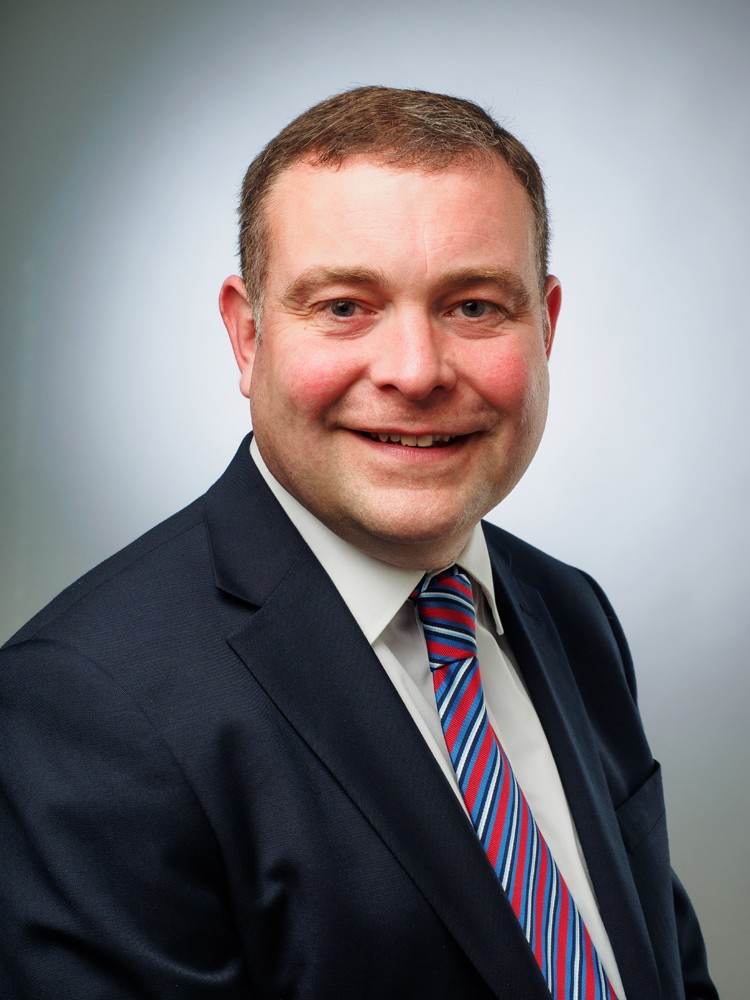 Business headshot of a smiling man in a navy suit and striped tie
