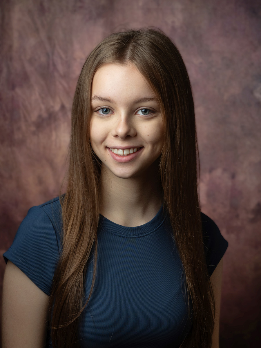 Headshot of a smiling teenage actor against a painted backdrop