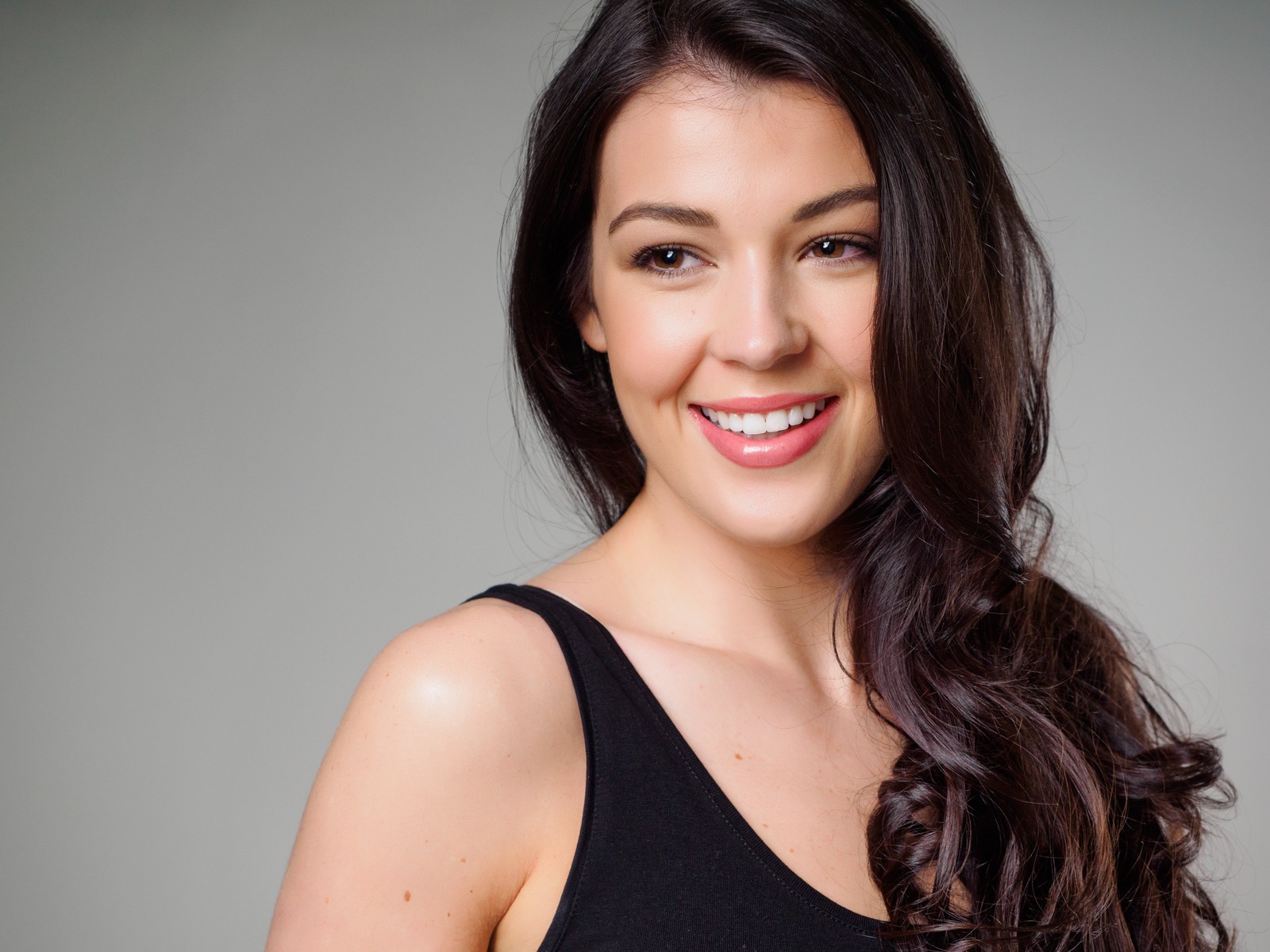 Smiling headshot of a woman in a black top on grey
