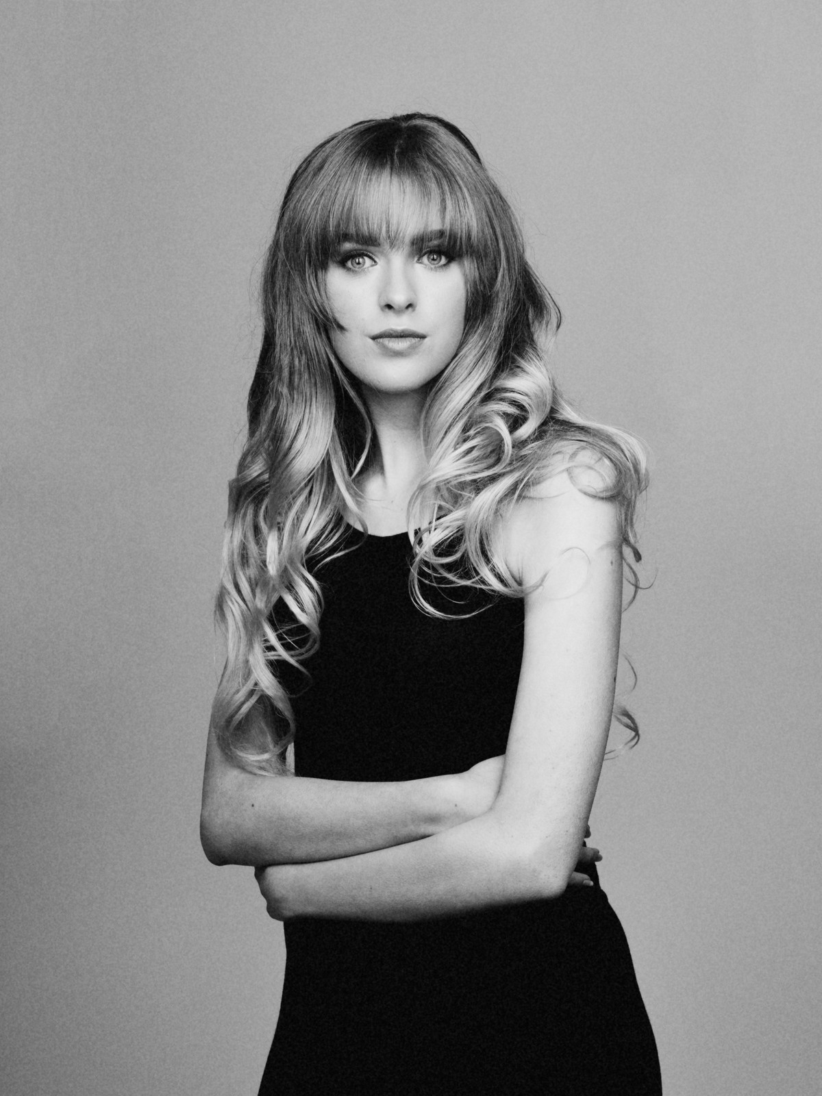 Young woman with a fringe and long curled hair, arms folded, black and white
