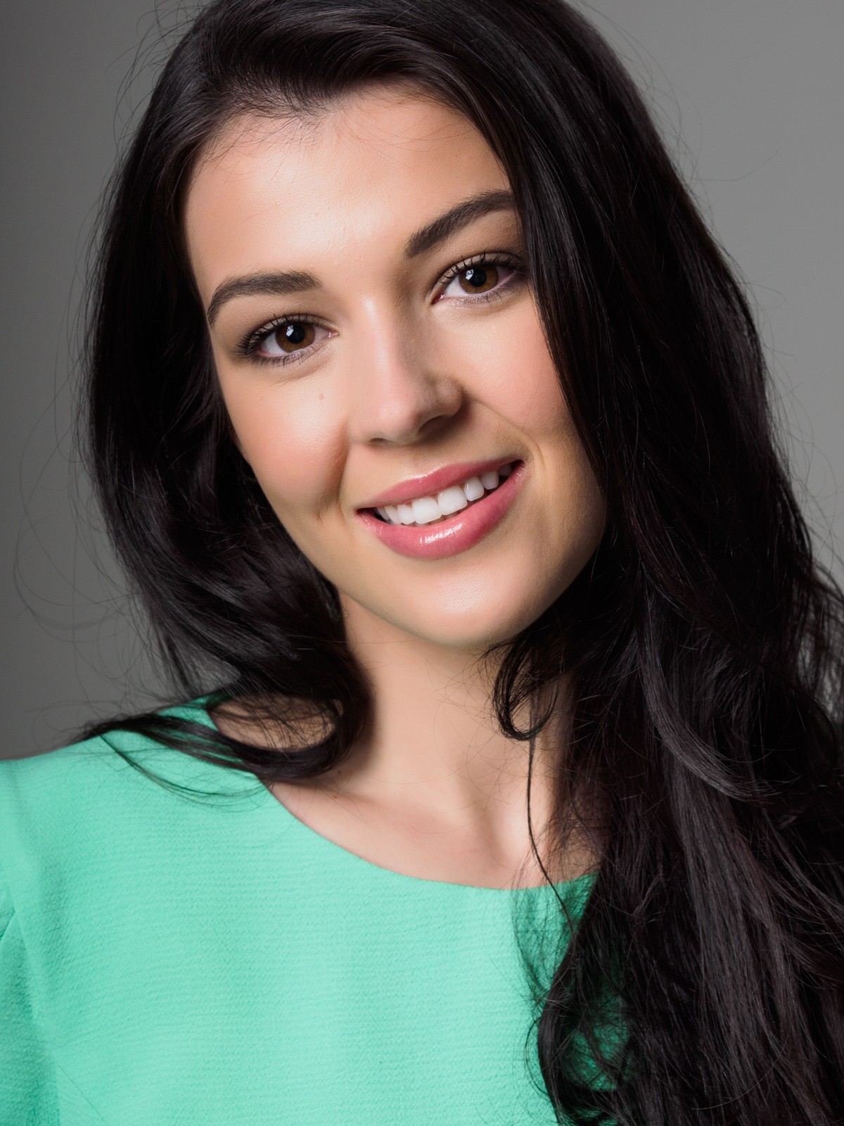 Smiling actor headshot of a woman with long dark hair on a grey background