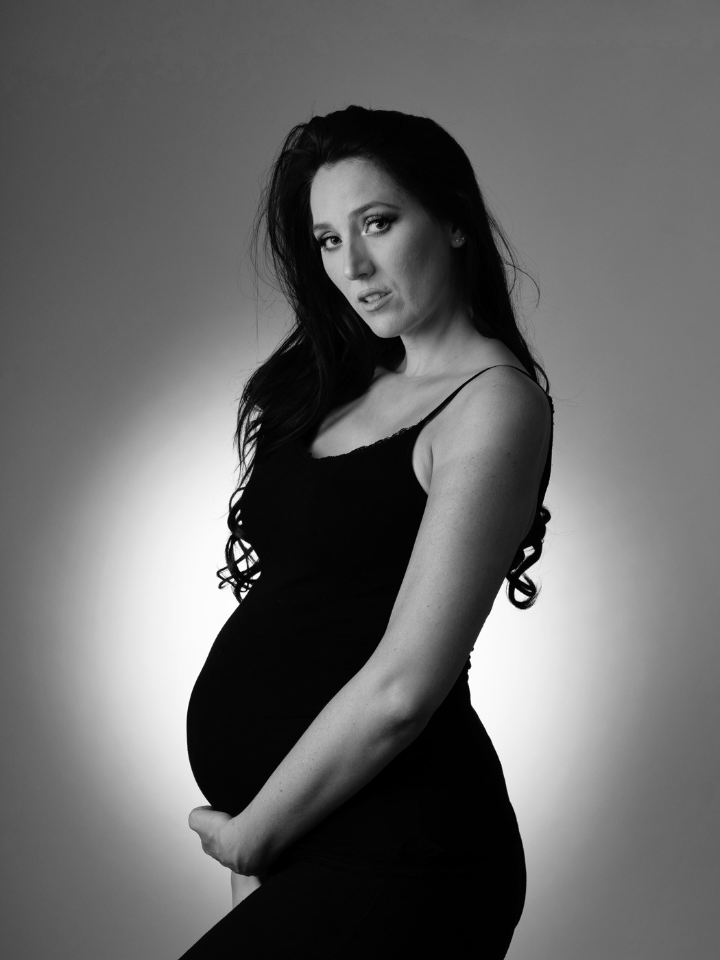 Mum-to-be in a black dress against a soft glow, black and white