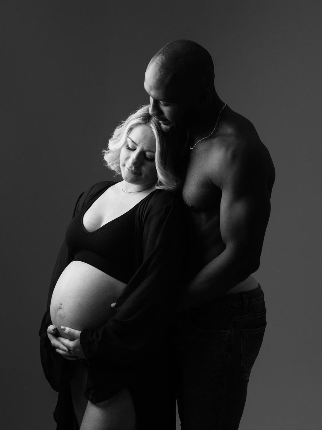 Couple embracing, her hands cradling the bump, black and white